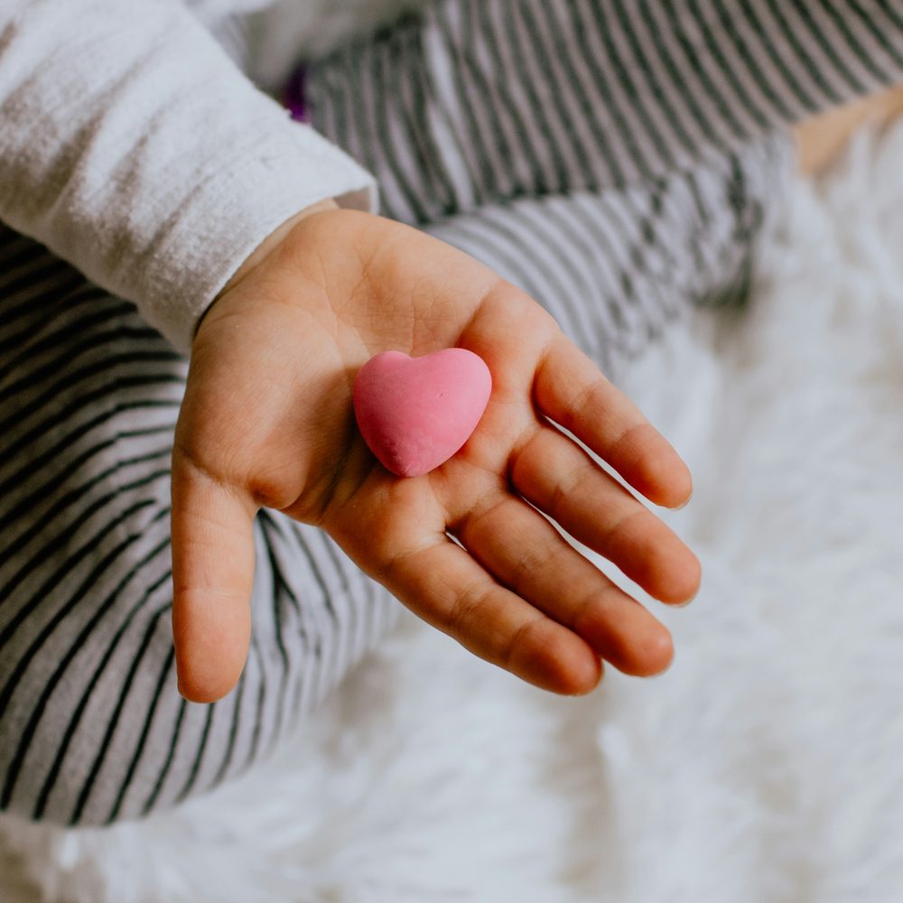 A child's open palm holding a small pink heart