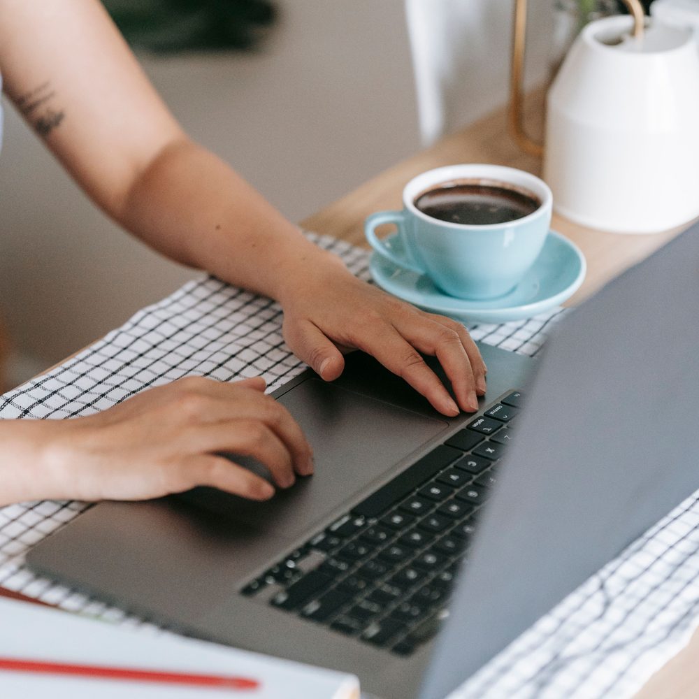 Hands typing on a laptop beside a cup of coffee